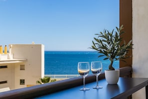 A balcony with two wine glasses and a potted plant, overlooking the sea.