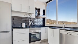 A modern kitchen with white cabinets, a black tiled backsplash, a built-in oven, and a large window offering a view of the landscape. - Casa Martin - Sea Views (Torremolinos)