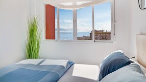 A bedroom with a bed, a window with a view of the sea and buildings, and a plant. - Casa Martin - Sea Views (Torremolinos)