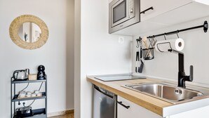 Una cocina compacta con microondas integrado, un lavabo y una cafetera en un estante.