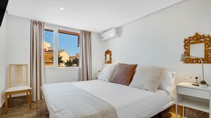 Una habitación de hotel moderna con una cama grande, una mesita de noche, una silla y una ventana con cortinas.