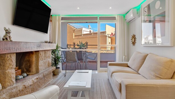Una sala de estar con chimenea, un sofá, un televisor montado en la pared y un balcón con vistas a edificios.