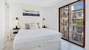 A bedroom with a large bed, a nightstand with a lamp, a wall-mounted painting, and a sliding glass door to a balcony. - Casa René - Pueblo Blanco (Torremolinos)
