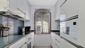 A modern kitchen with white cabinetry, stainless steel appliances, and a window with blinds. - Casa René - Pueblo Blanco (Torremolinos)