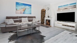 A modern living room with a sofa, coffee table, fireplace, and a flat-screen TV. - Casa René - Pueblo Blanco (Torremolinos)