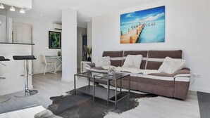 A modern living room with a brown sofa, a glass coffee table, and a large painting of a pier. - Casa René - Pueblo Blanco (Torremolinos)