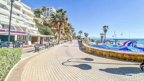 Um calçadão à beira-mar com um caminho de tijolos curvo, palmeiras e guarda-sóis de praia.