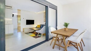 Um espaço de estar moderno com área de jantar, sofá, televisão e cozinha visível através de um painel de vidro.