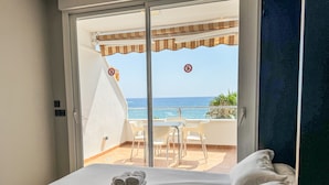 Ett hotellrum med en säng, en balkong med ett bord och stolar samt utsikt över havet.