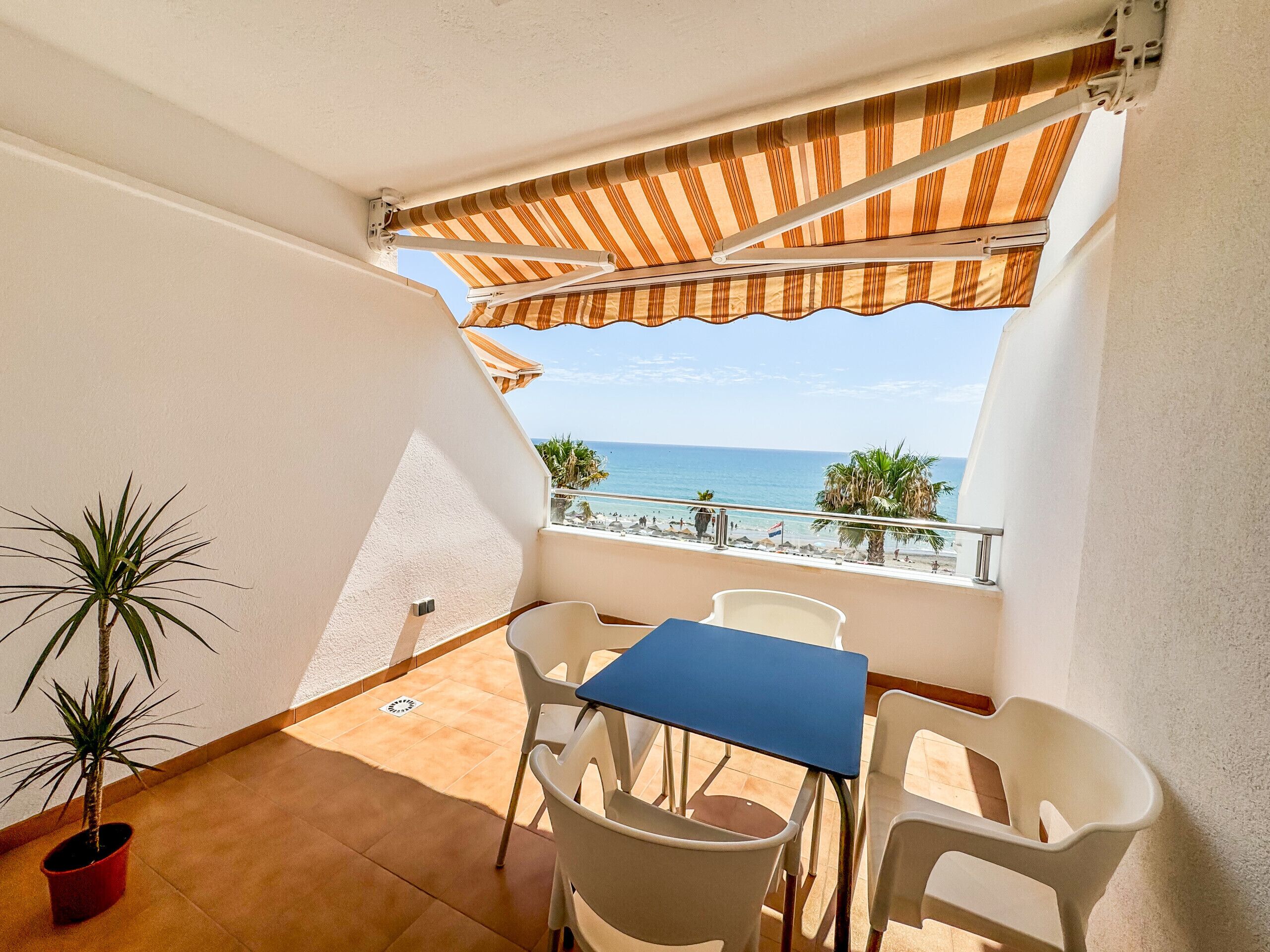 Un balcon avec une table et des chaises, un pot de fleurs et une vue sur la plage et l’océan.