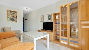 Un salon moderne comprenant un canapé, une table basse, un téléviseur et un meuble vitré contenant de la vaisselle.