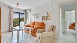 Un salon moderne avec un canapé, une table basse et une vue dégagée sur l’extérieur grâce à une grande fenêtre.