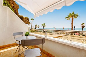 En balkon med udsigt over stranden, med et bord, stole, en potteplante og gelænder.