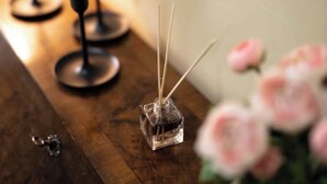 A small square glass bottle with reed sticks, placed on a wooden surface. - Aretina Apartment Cozy (Firenze)