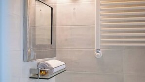 A modern bathroom with a glass shelf holding a towel and a small container, a mirror, and a toilet with a flush handle. - Aretina Apartment Cozy (Firenze)