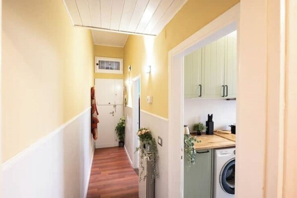Un pasillo estrecho con suelo de madera, una lavadora y un armario en una zona de cocina.