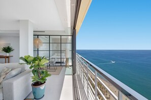 A balcony with a view of the ocean and a modern interior with a sofa, potted plants, and a dining area.