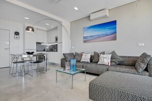 Un salón moderno con una mesa de centro de vidrio, un sofá gris y un cuadro de una playa.