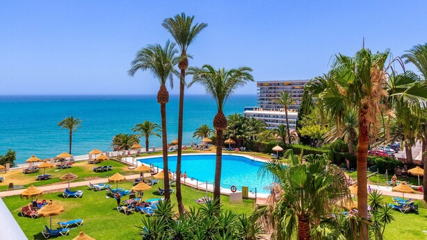 A resort with a pool, palm trees, and a view of the ocean.