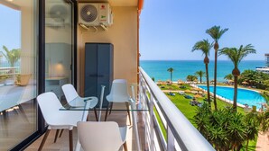 A balcony with a glass table and chairs, overlooking a pool and palm trees.