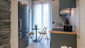 A compact kitchen with a refrigerator, a dining table with chairs, a small island with a sink, and a window with sheer curtains. - Pratellino Florence Apartment (Firenze)