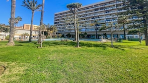 Un hotel de varios pisos con una zona de piscina, rodeado de palmeras y un césped bien cuidado.
