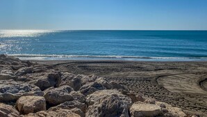 Una playa con grandes rocas en primer plano y un cielo azul despejado.