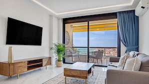 Una sala moderna con televisor de pantalla plana, mueble de madera para equipo multimedia, una mesa de centro, un sofá y un balcón con mobiliario exterior.