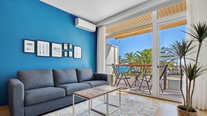 Ein Wohnzimmer mit grauem Sofa, Couchtisch und großem Fenster mit Blick auf Palmen und einen Balkon.