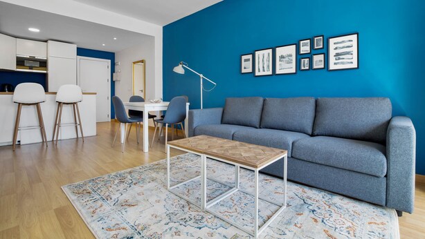 A modern living room with a blue accent wall, a grey sofa, a wooden coffee table, and a patterned rug. - Casa Jiri - Sea Views (Torremolinos)