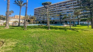 Ein mehrstöckiges Hotel mit Poolanlage, umgeben von Palmen und einem gepflegten Rasen.