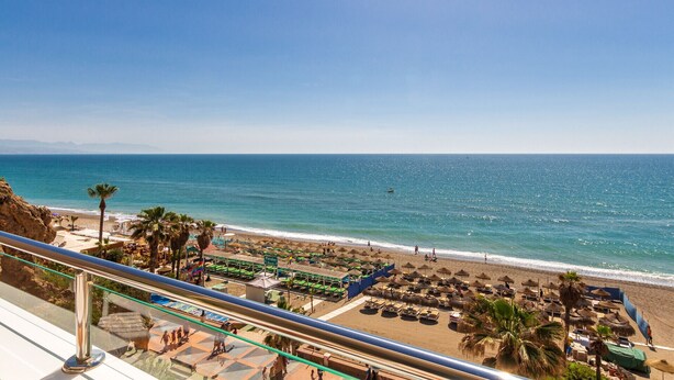 A beach with umbrellas and lounge chairs, a clear sky, and the ocean.