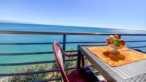 Ein Balkon mit Tisch und Stühlen, mit Blick auf ein klares blaues Meer und entfernte Berge.