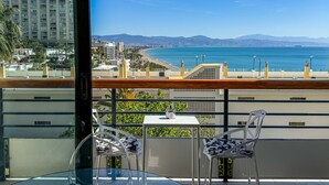A balcony with a view of the sea, a table, and two chairs.