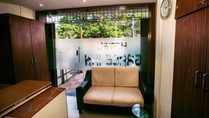 A compact room with a sofa, a small table, and a view through a barred window. - Hotel Grace Executive (Mumbai)