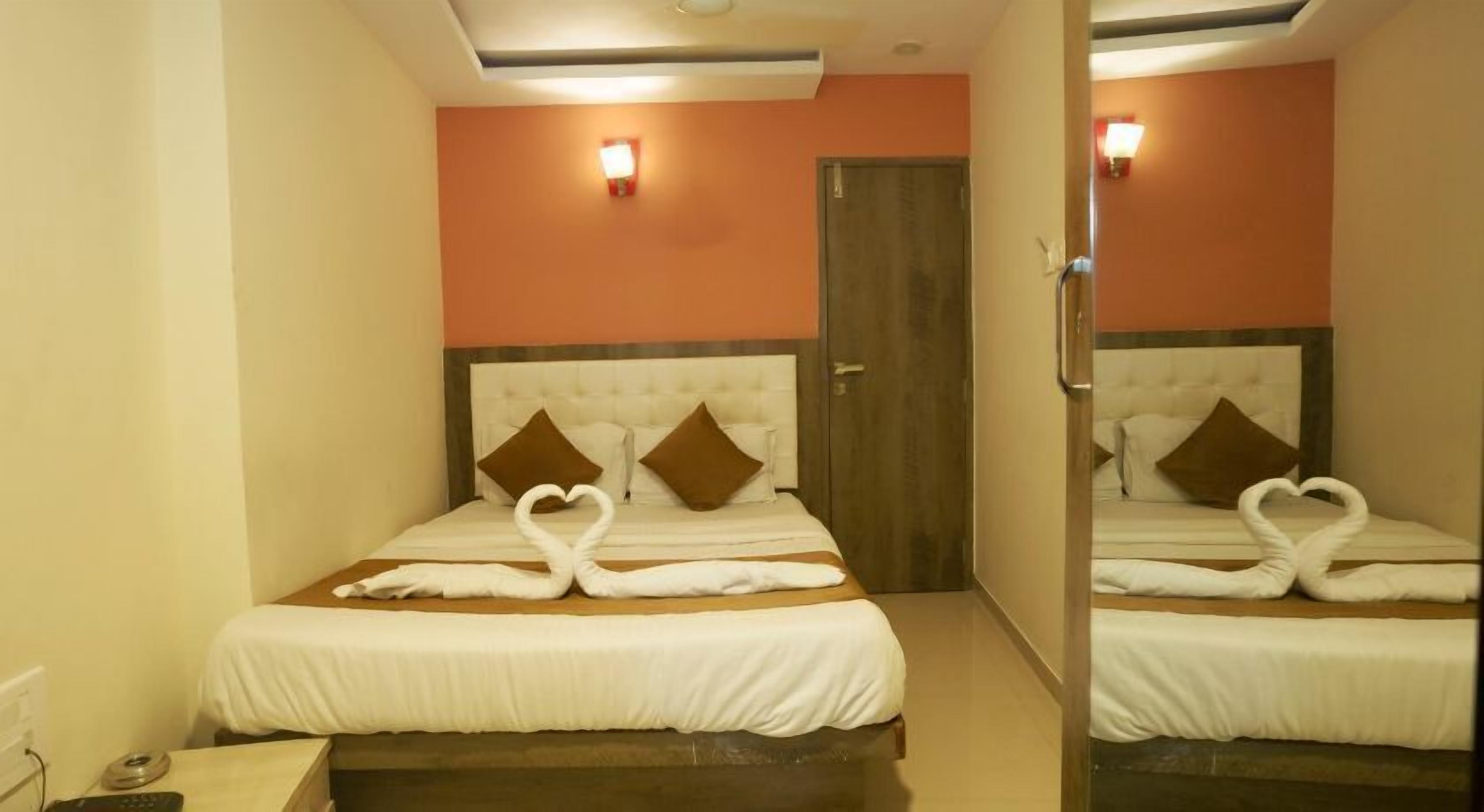 Quarto de hotel com duas camas, cada uma com toalhas dispostas em formato de coração, uma porta de madeira e um espelho refletindo o quarto.