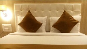 A neatly made bed with a tufted headboard and two brown pillows. - Hotel Grace Executive (Mumbai)