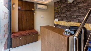 A hotel room with a wooden wardrobe, a bench, a reception desk, and a stone wall. - Hotel Grace Executive (Mumbai)