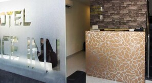 Ein Empfangsbereich mit modernem Design, inklusive einer Glaswand mit der Aufschrift "HOTEL" und einer Wand mit Musterung.