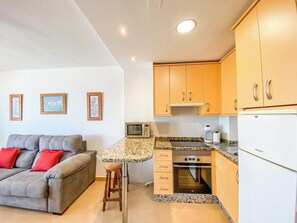A compact living space with a kitchenette, a grey sofa with red cushions, and framed pictures on the wall. - Casa Ángela - Sea views (Torremolinos)