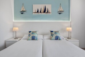 Een tweepersoonsbed met bijpassende kussens, twee bedlampjes en een schilderij van zeilboten op de muur.