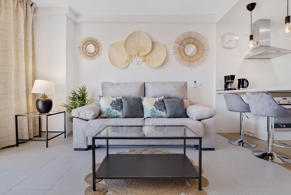 A modern living room with a sofa, coffee table, and a kitchen area with bar stools.