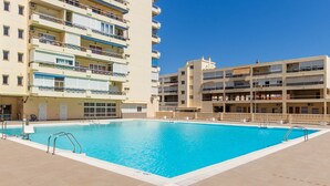 A swimming pool surrounded by multi-story buildings with balconies. - Casa Hugo - La Carihuela (Torremolinos)