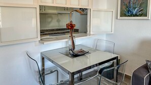 A modern kitchen with white cabinets, a glass table, and clear chairs. - Casa Hugo - La Carihuela (Torremolinos)