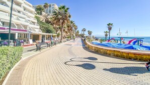 Un paseo marítimo adoquinado con bancos, palmeras y vista al mar.