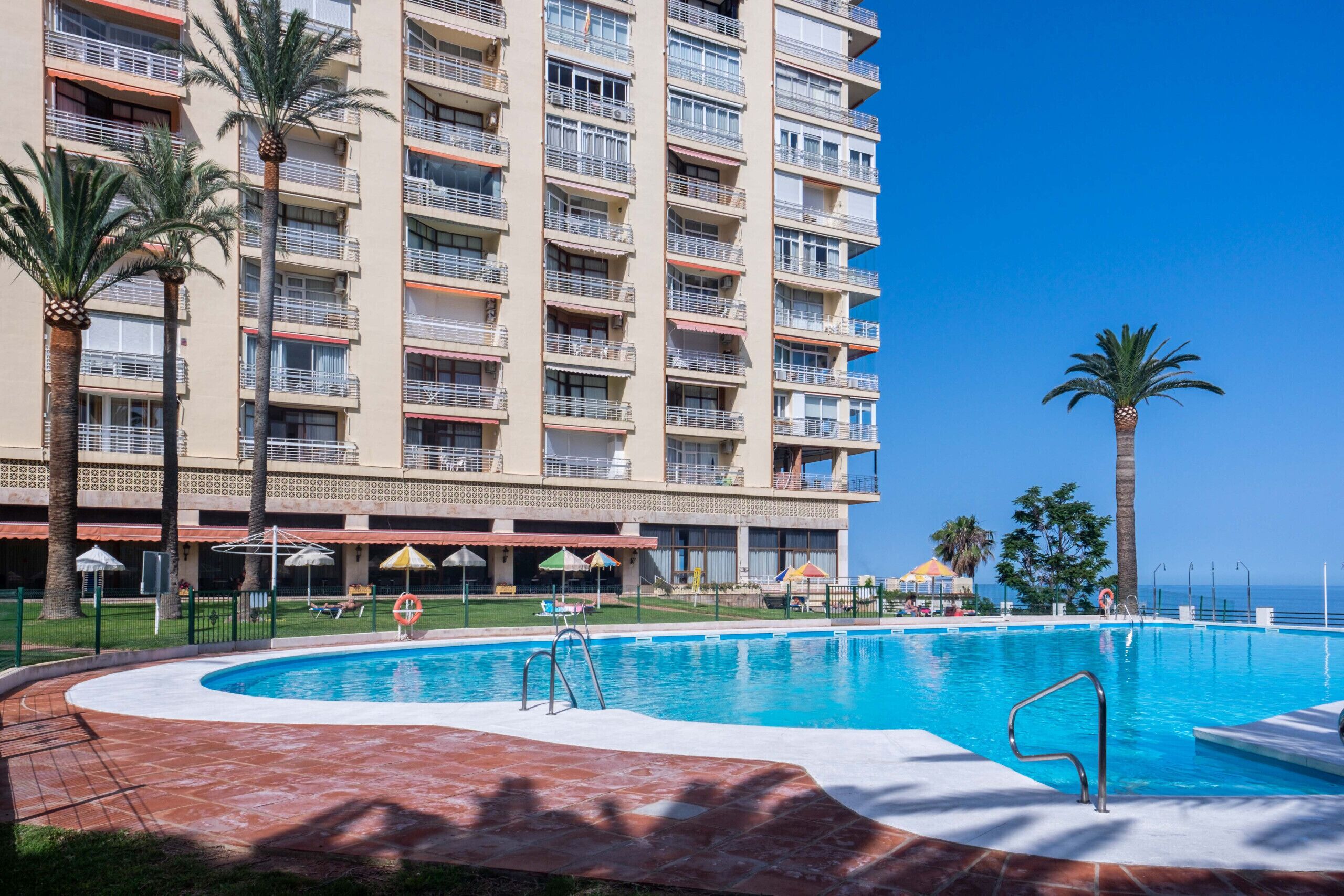 A hotel with a large pool, palm trees, and a clear blue sky.