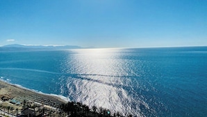 Une plage offrant une vue dégagée sur l’océan et les montagnes lointaines, le tout baigné par un soleil éclatant.