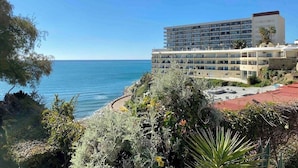 Un hôtel situé sur la côte, avec plusieurs étages, un parking à toit rouge et une vue sur la mer.