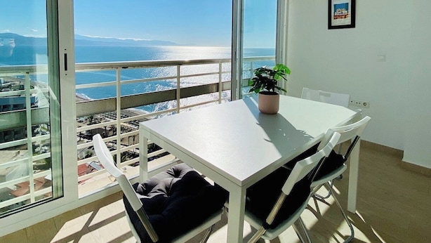 Un balcon avec une table et des chaises, une plante en pot et un tableau encadré au mur.