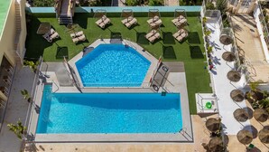 An octagonal pool with a surrounding deck, lounge chairs, and a small seating area with tables and umbrellas.